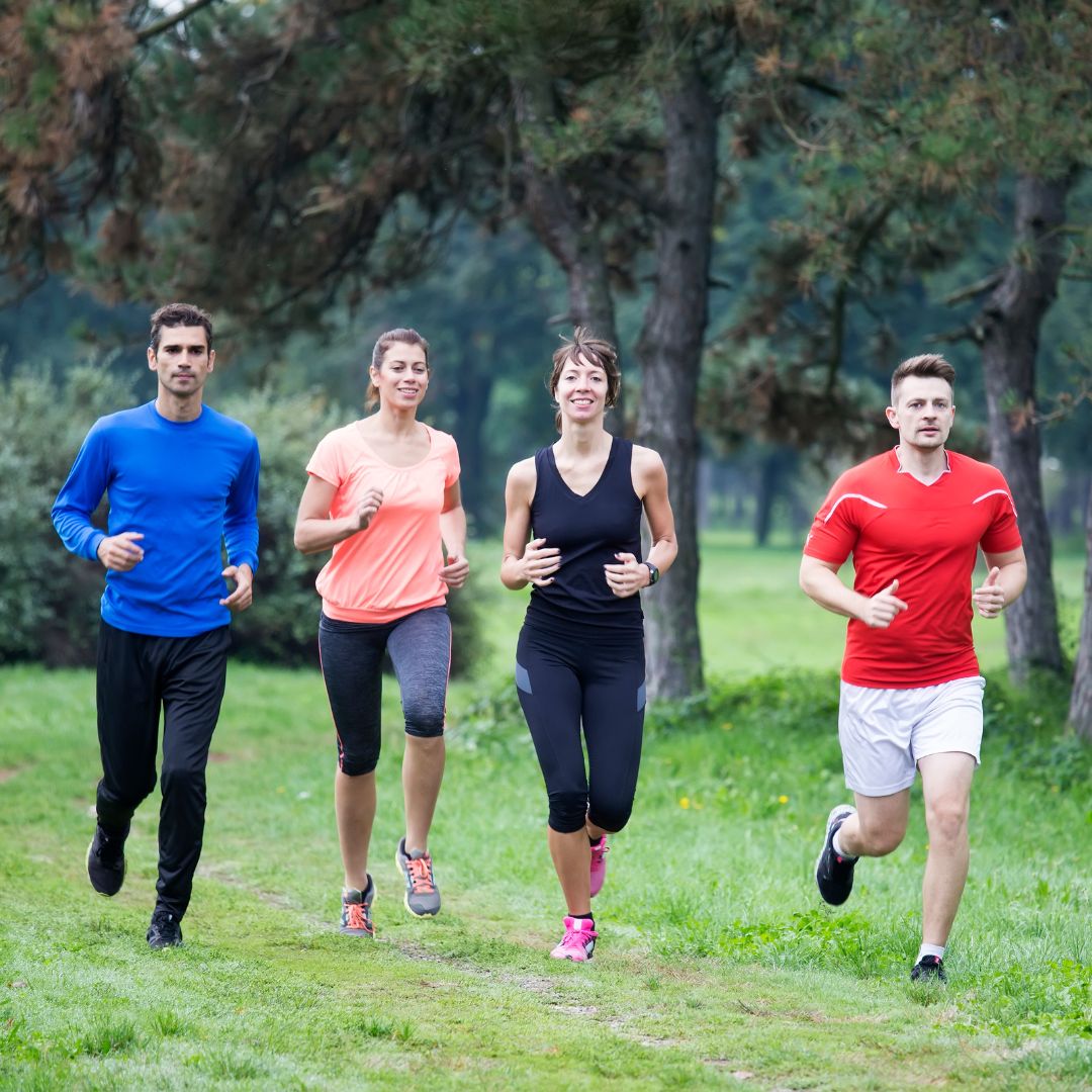 Happy group of friends running together outdoors in park during morning fitness workout