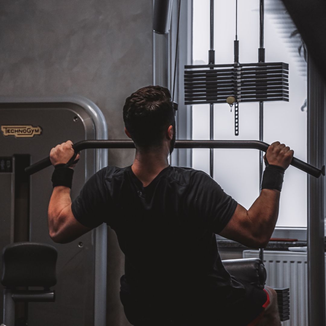 Muscular man performing lat pulldown exercise on cable machine in professional gym