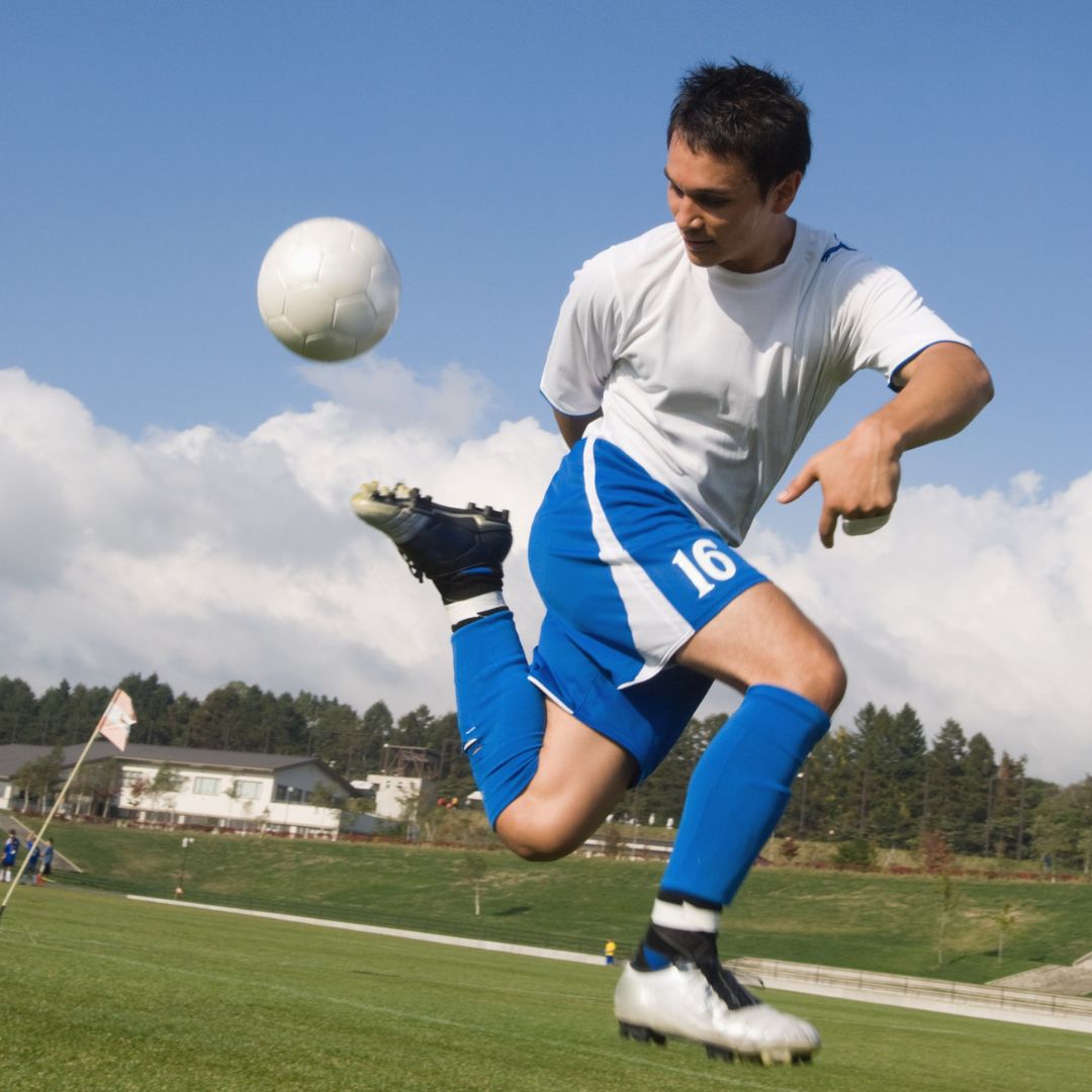 Young man performing powerful soccer kick with ball in mid air on sports field